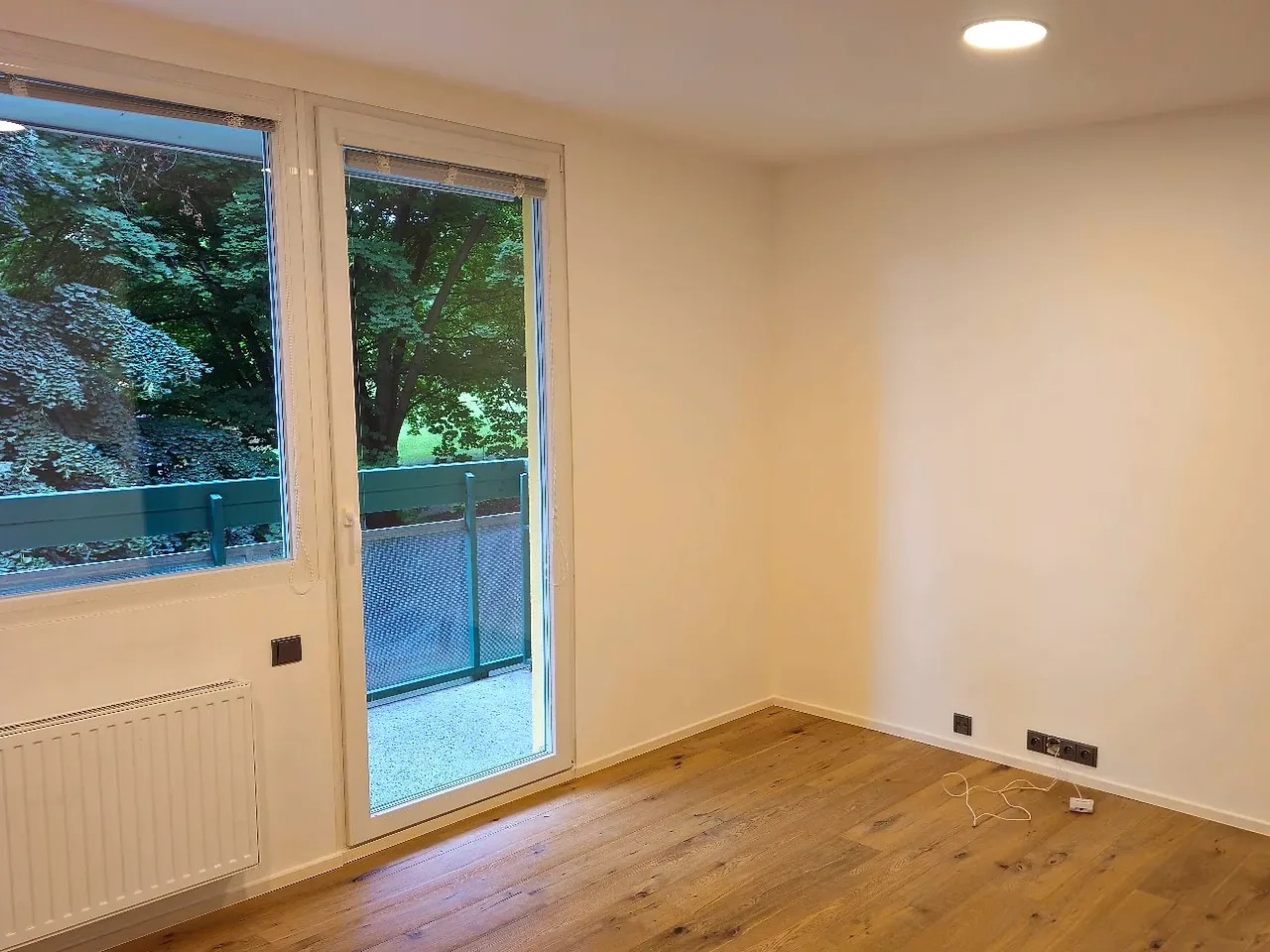 Světlý pokoj po dokončené rekonstrukci s dřevěnou podlahou a vstupem na balkon
