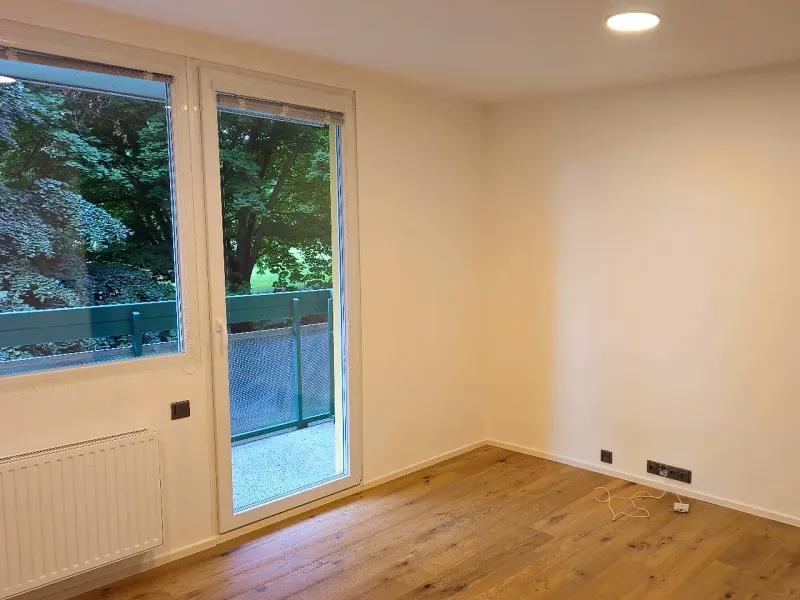 Světlý pokoj po rekonstrukci s dřevěnou podlahou a vstupem na balkon